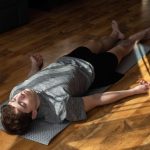 Ein junger Mann liegt auf dem Holzboden und macht den Bodyscan