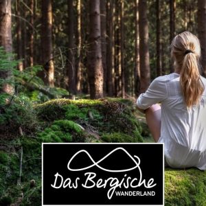 Eine blonde Frau mit langem Pferdeschwanz sitzt beim Workshop im Wald und meditiert